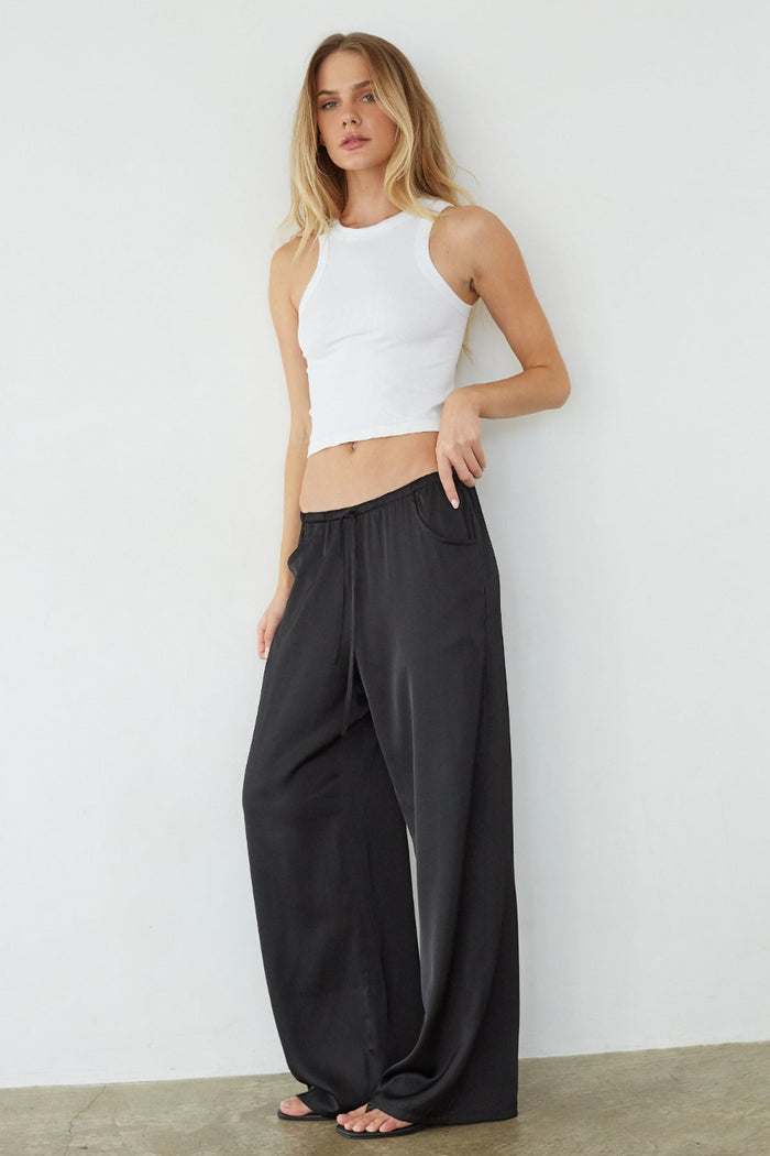 Woman wearing a white sleeveless top and black wide-leg pants against a plain background