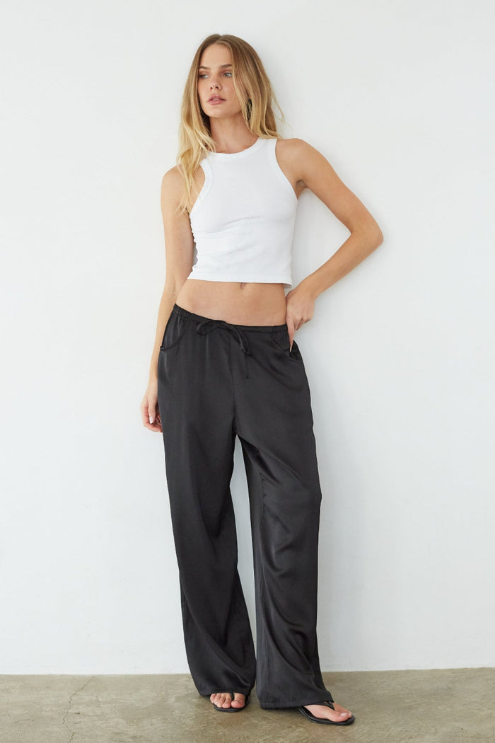 Woman wearing a white crop top and black wide-leg pants against a plain white wall.