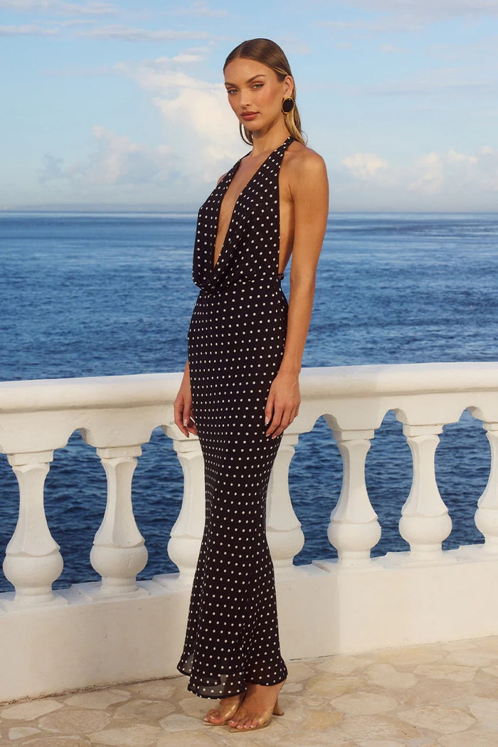 Woman in a black polka dot dress standing on a balcony with ocean view