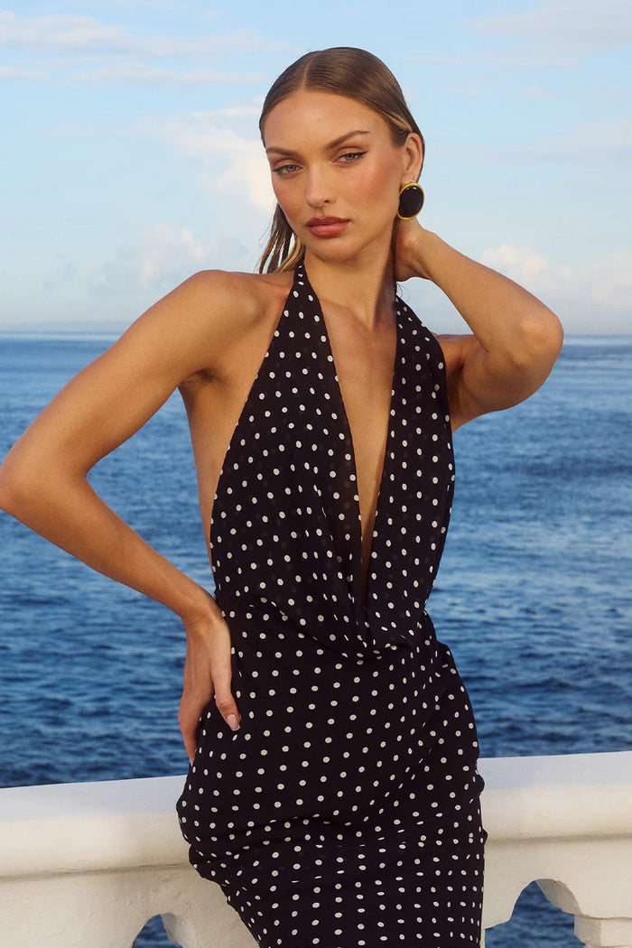 Woman wearing a black polka dot dress with a deep neckline by the ocean.