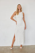 Woman wearing a white sleeveless dress with a slit on a plain background