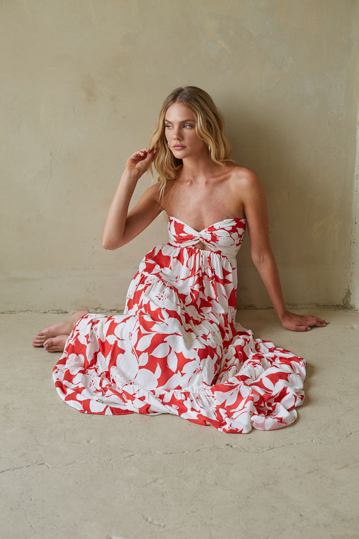 Woman in a strapless red and white floral dress sitting against a plain wall.