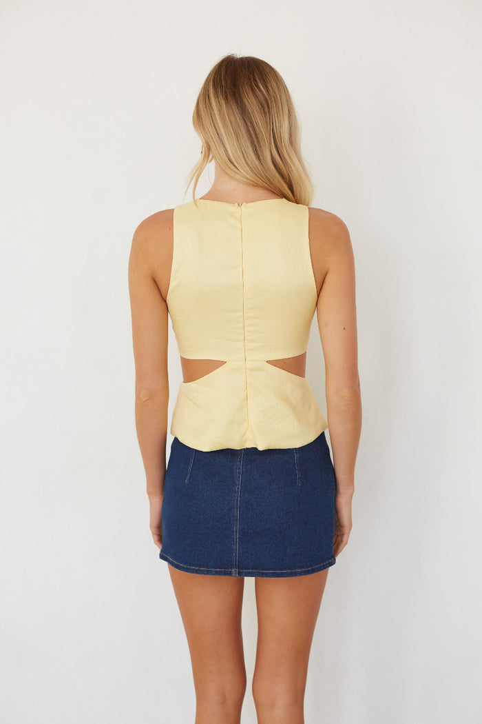 Woman wearing a yellow sleeveless top with cut-out design and a blue denim skirt on a white background