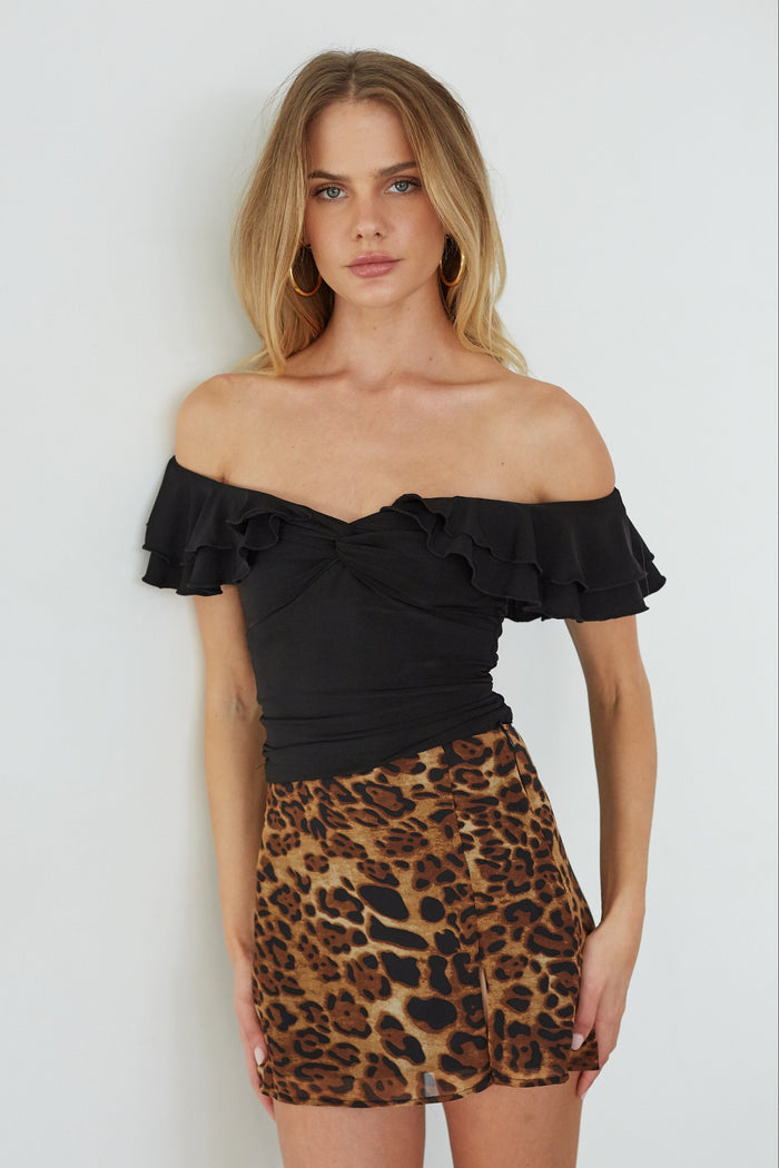 Woman wearing a black off-shoulder top and leopard print skirt against a white background