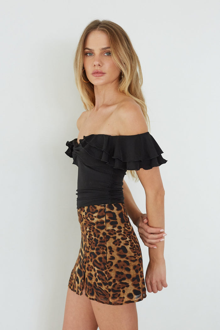 Woman wearing a black off-shoulder top and leopard print skirt on a white background