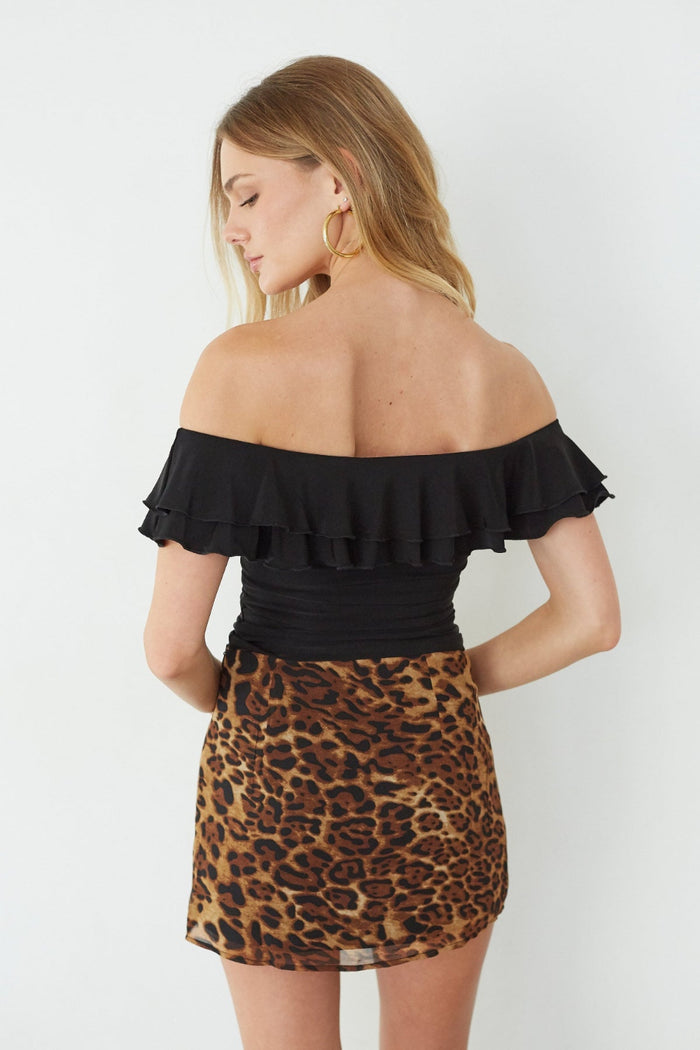 Woman wearing a black off-shoulder top and leopard print skirt on a white background