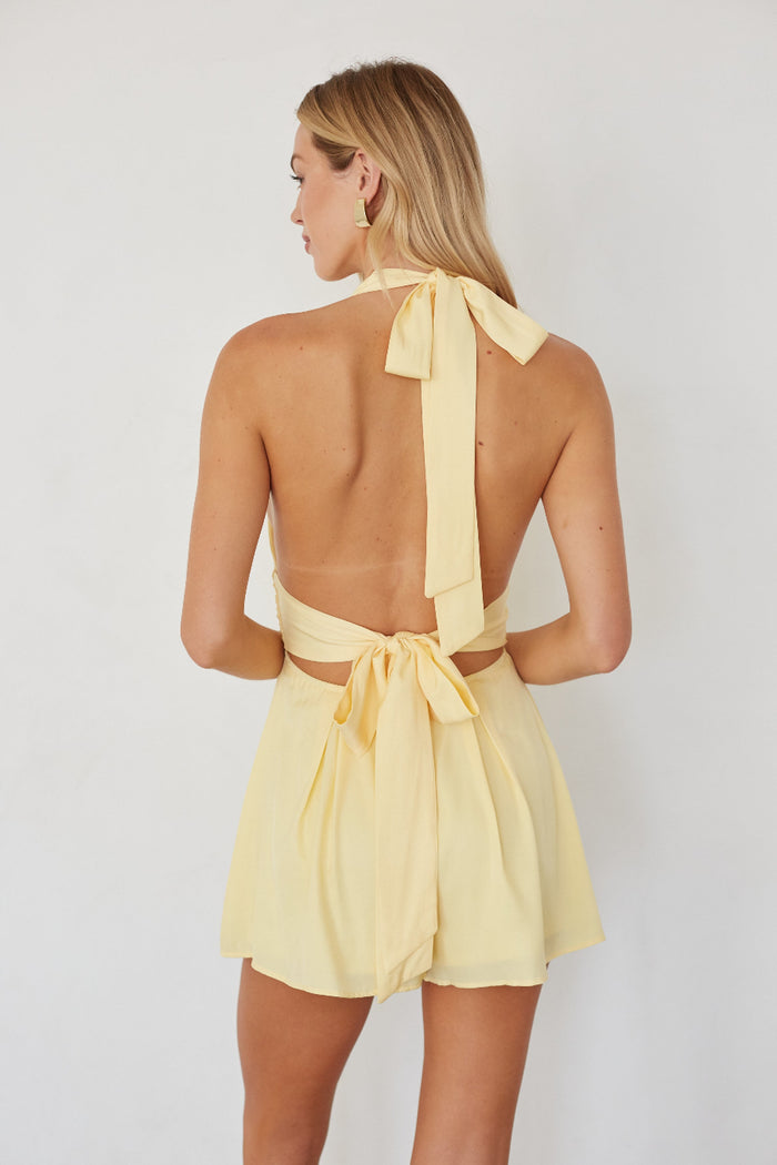Woman wearing a yellow dress with a halter neck and open back on a white background