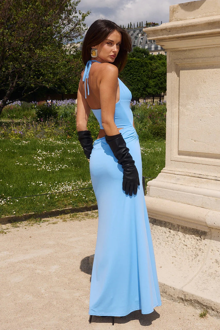 Woman in a light blue evening gown with black gloves standing outdoors.