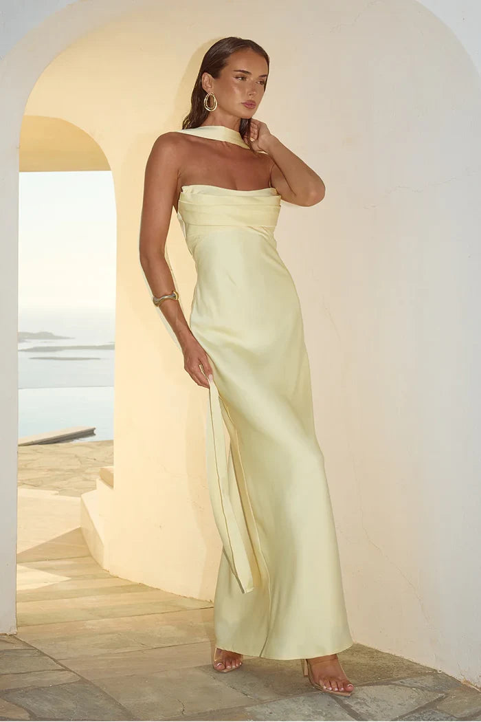 Woman in a strapless light yellow dress standing in a sunlit room with a white wall and wooden floor.
