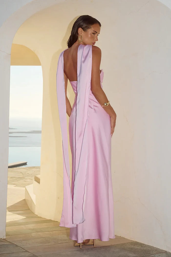 Woman in a pink dress with a flowing train standing in a sunlit archway.