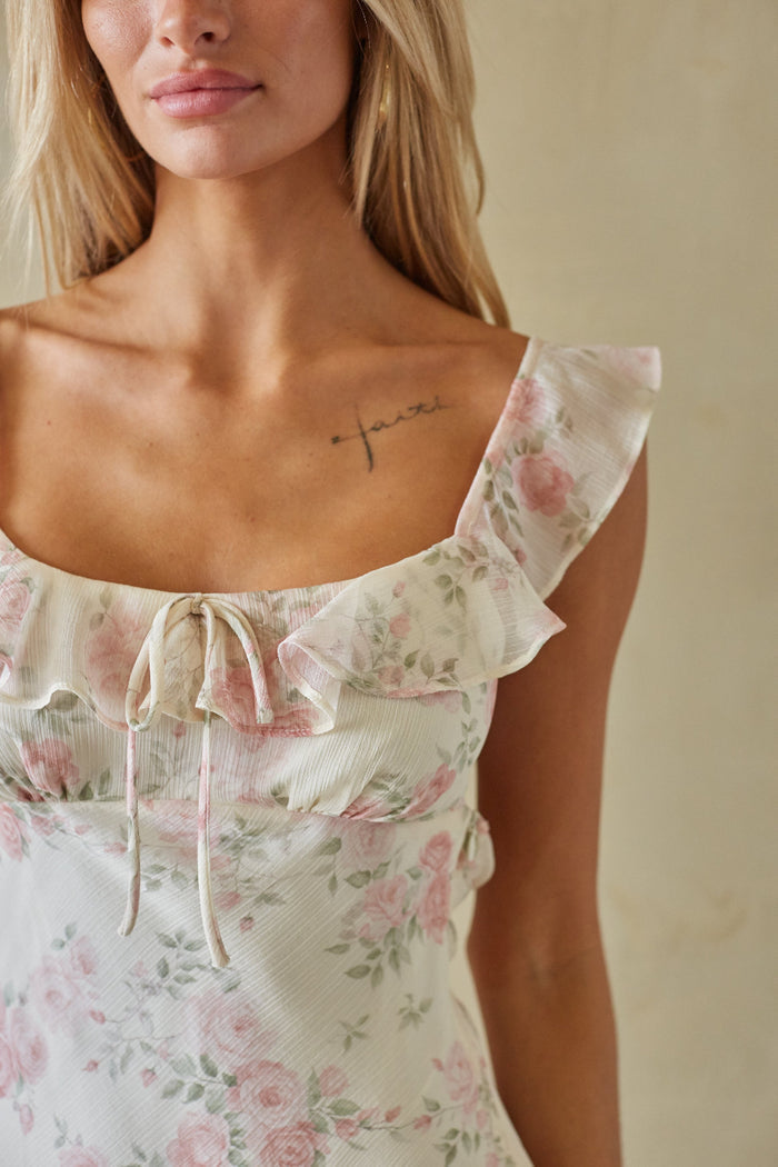 Woman wearing a floral dress with ruffled shoulders against a neutral background