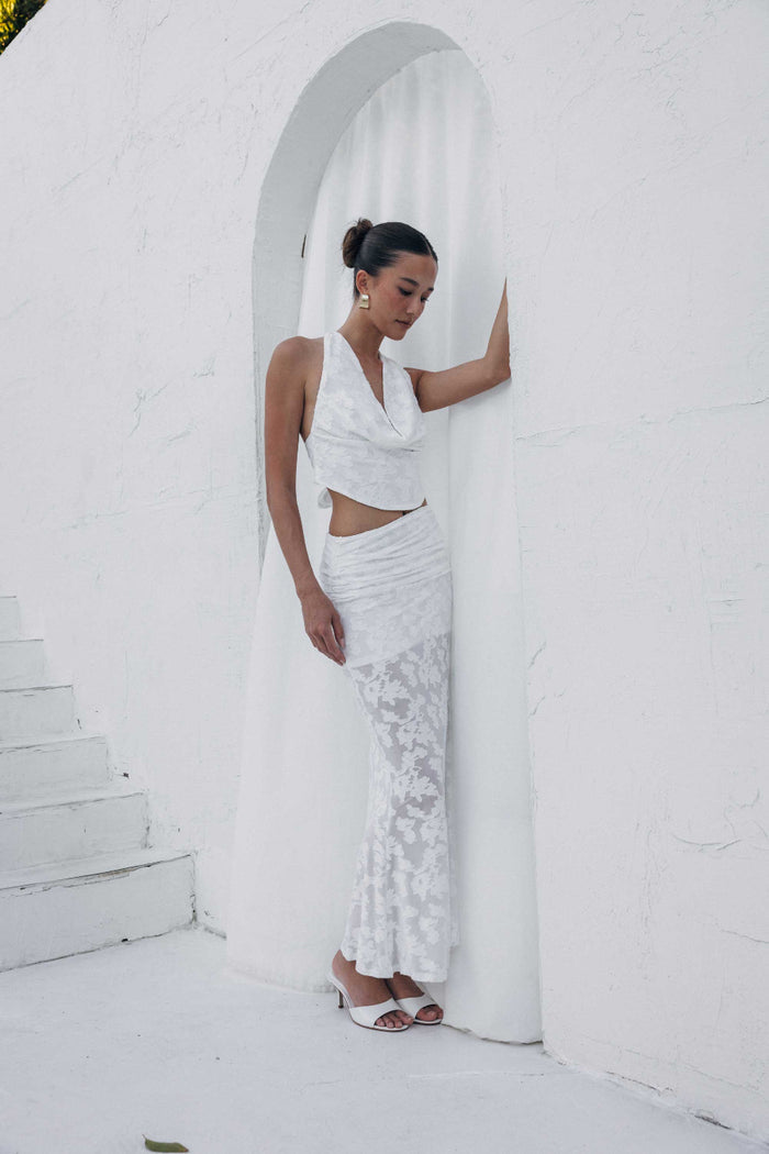 Woman in a white outfit standing against a white wall with an arch.