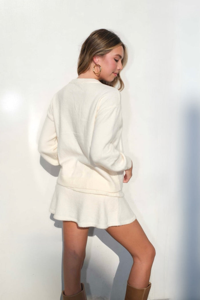 Image of a girl in a cream colored cardigan. The girl is turned around to show the back.