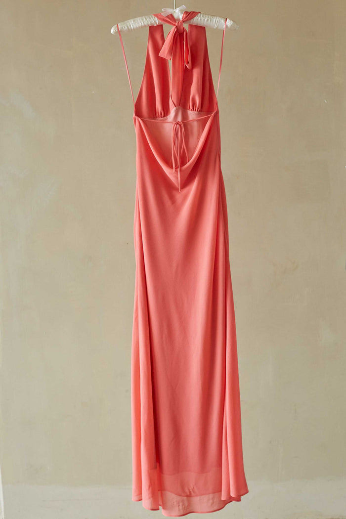 Coral evening gown on a beige hanger against a beige background