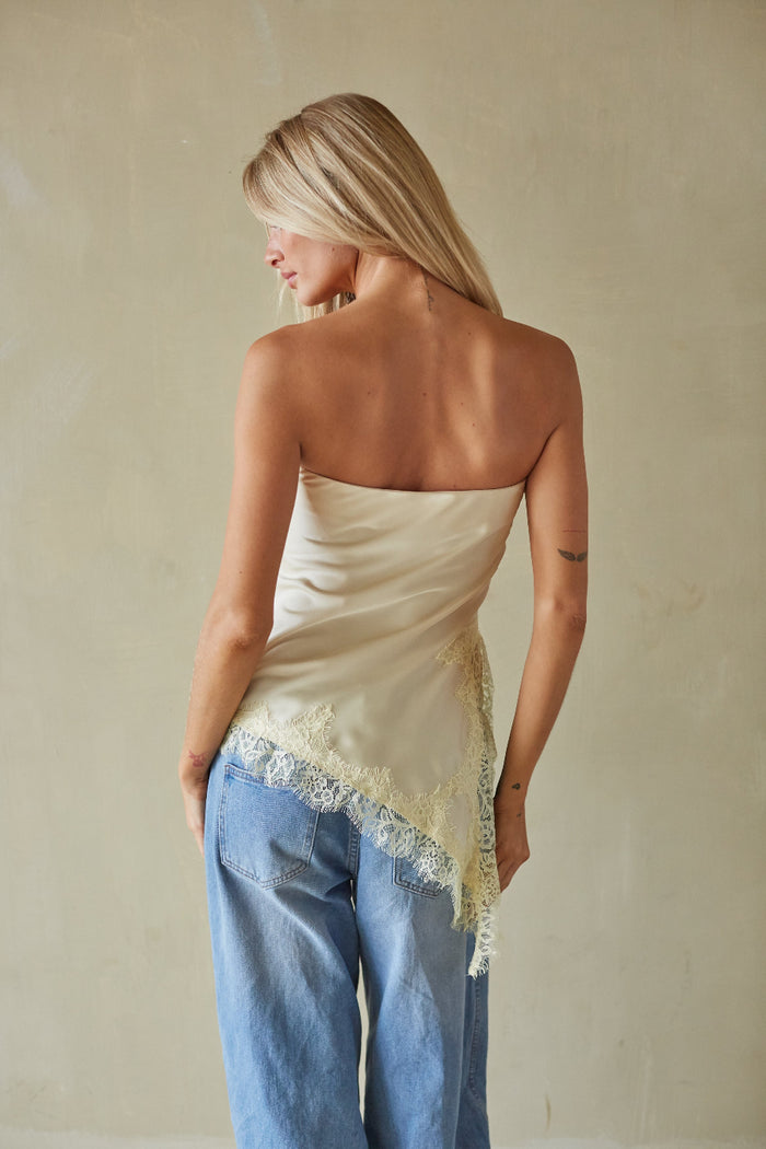 Woman wearing a strapless top with lace trim and blue jeans against a beige background