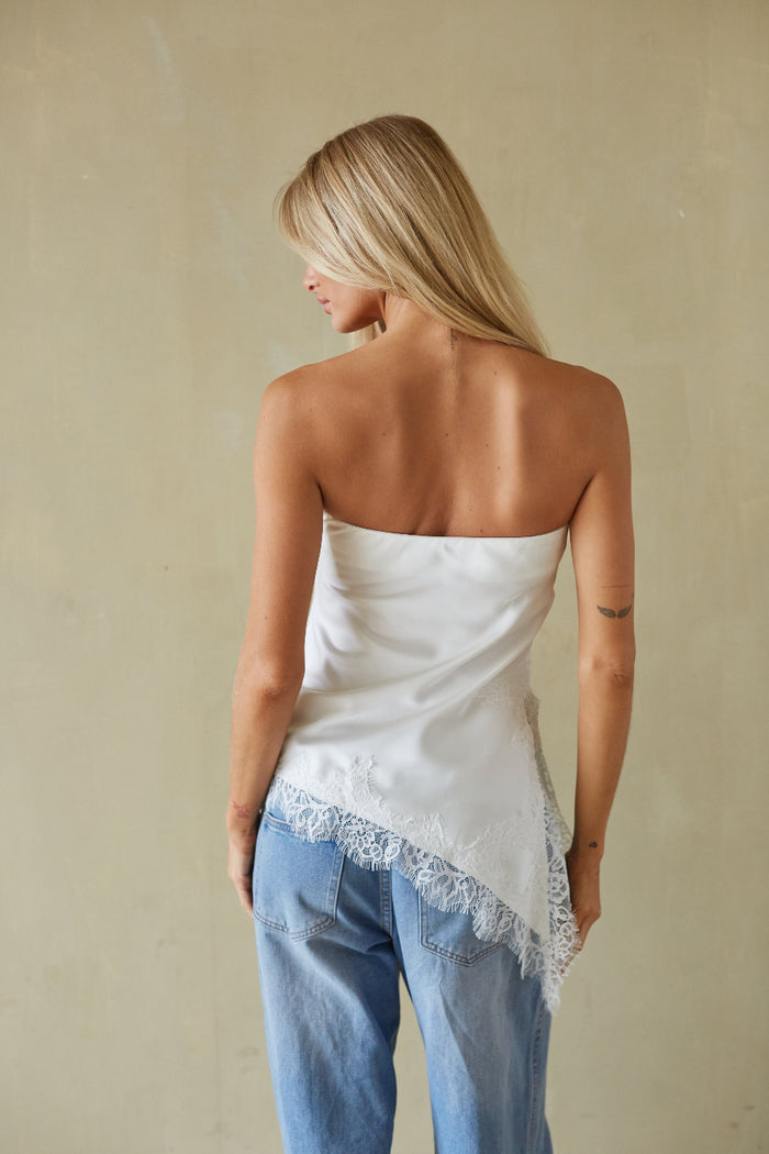Woman wearing a strapless top with lace trim and blue jeans against a beige background