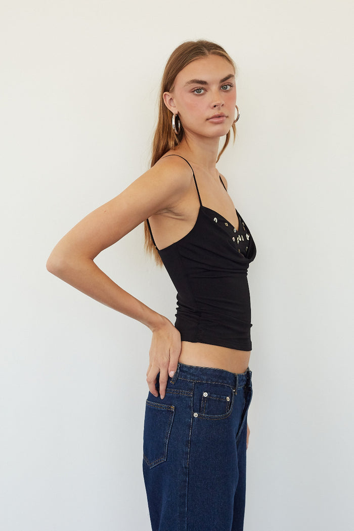 A woman modeling a black spaghetti-strap crop top with silver rhinestone embellishments on the cups, paired with dark blue jeans, against a plain white studio background.