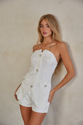 A woman wearing a white strapless bustier top with rhinestone embellished buttons and faux front flap pockets, paired with matching tailored shorts. Both pieces are fully lined and appear to be bridal wear.