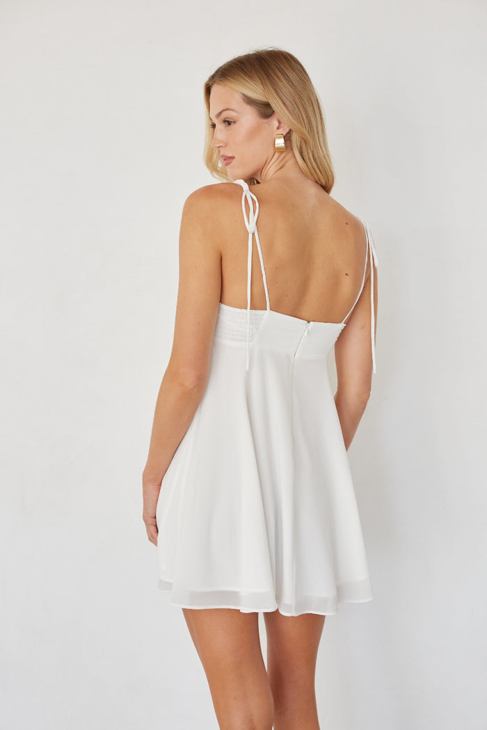 Woman wearing a white dress with thin straps on a plain background