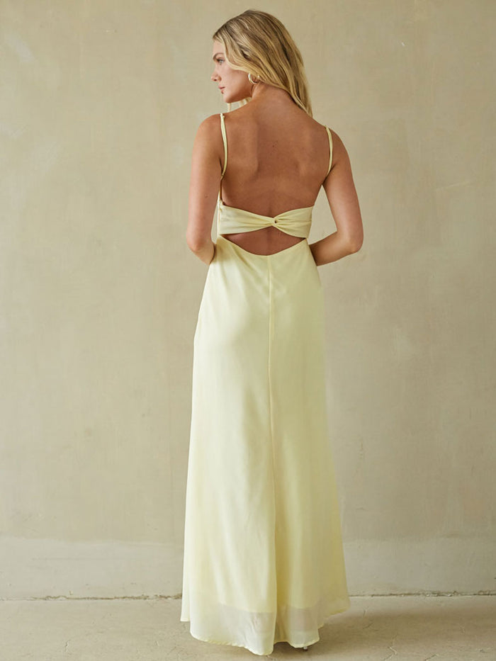 Woman wearing a light yellow dress with cut-out back against a beige background
