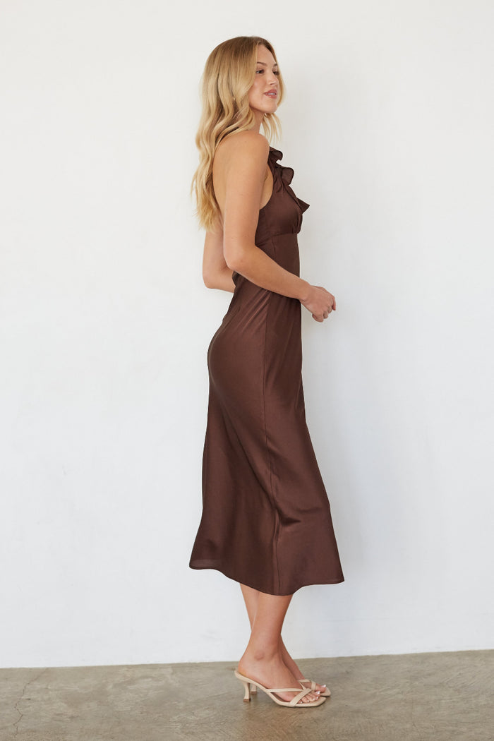 Woman wearing a brown dress standing against a white wall.