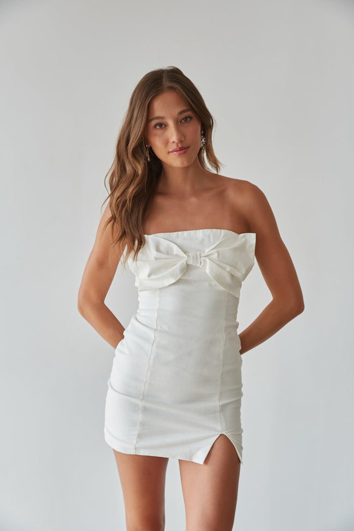 A woman in a white strapless mini dress with bow detail, perfect for formal mini dresses or hoco dresses.
