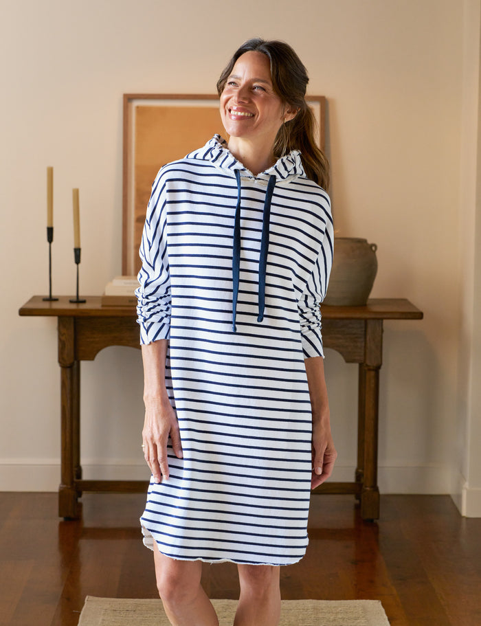 Woman wearing a blue and white striped dress standing in a room with wooden furniture.