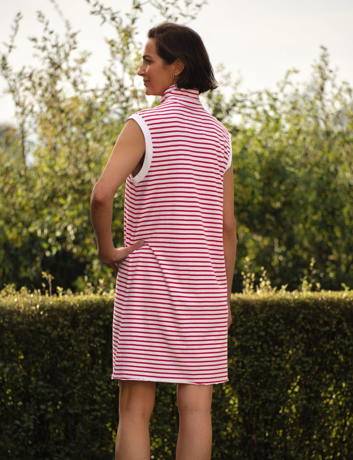 Woman wearing a red and white striped dress standing outdoors with greenery in the background