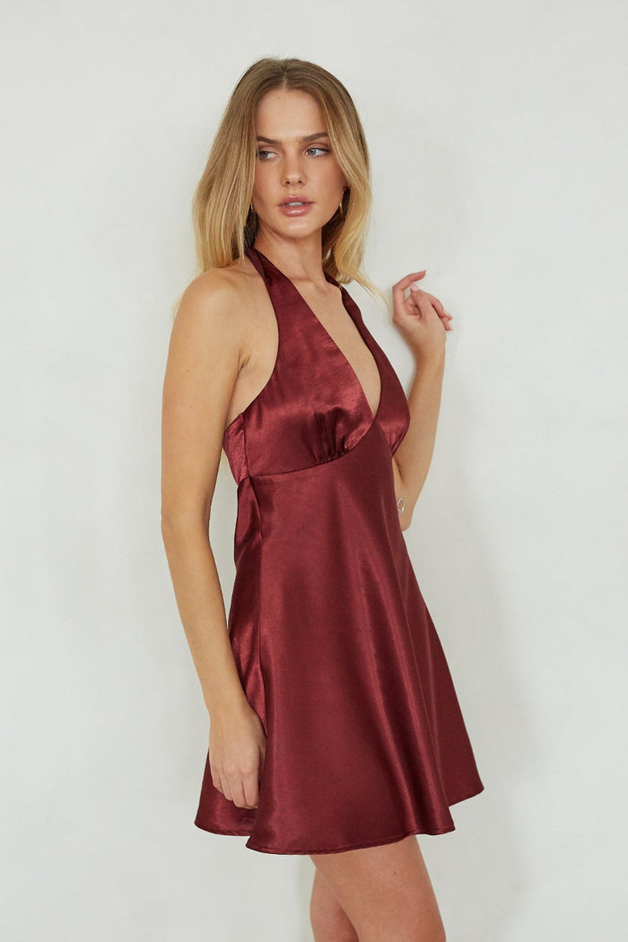 Woman wearing a burgundy satin halter neck dress against a white background