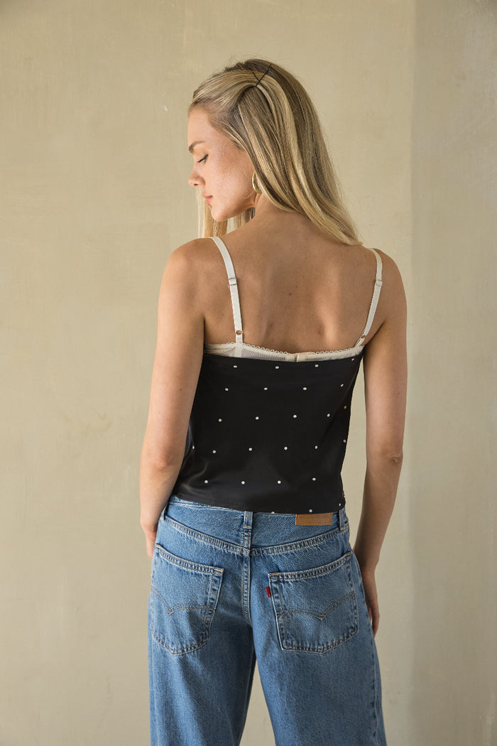 Woman wearing a black polka dot top and blue jeans against a beige background