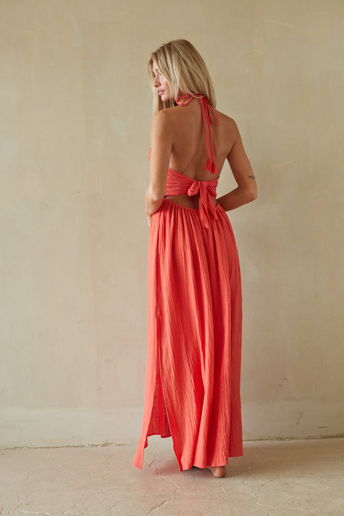 Woman wearing a coral halter neck dress against a plain background