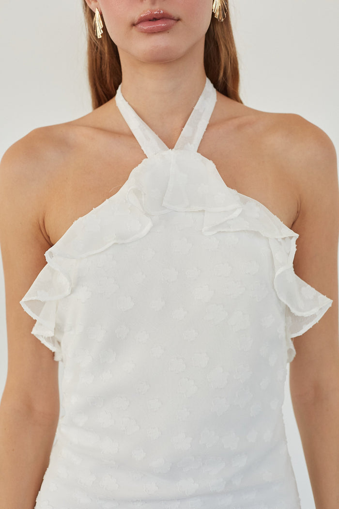 A close-up of a model wearing a white halter top with ruffled details and a subtle textured pattern, set against a plain light background.