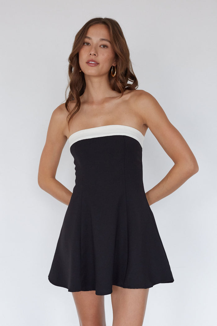Woman wearing a black strapless dress with a white top on a plain background