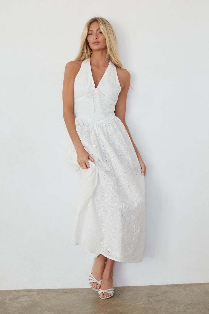 Woman wearing a white halter neck dress against a plain background