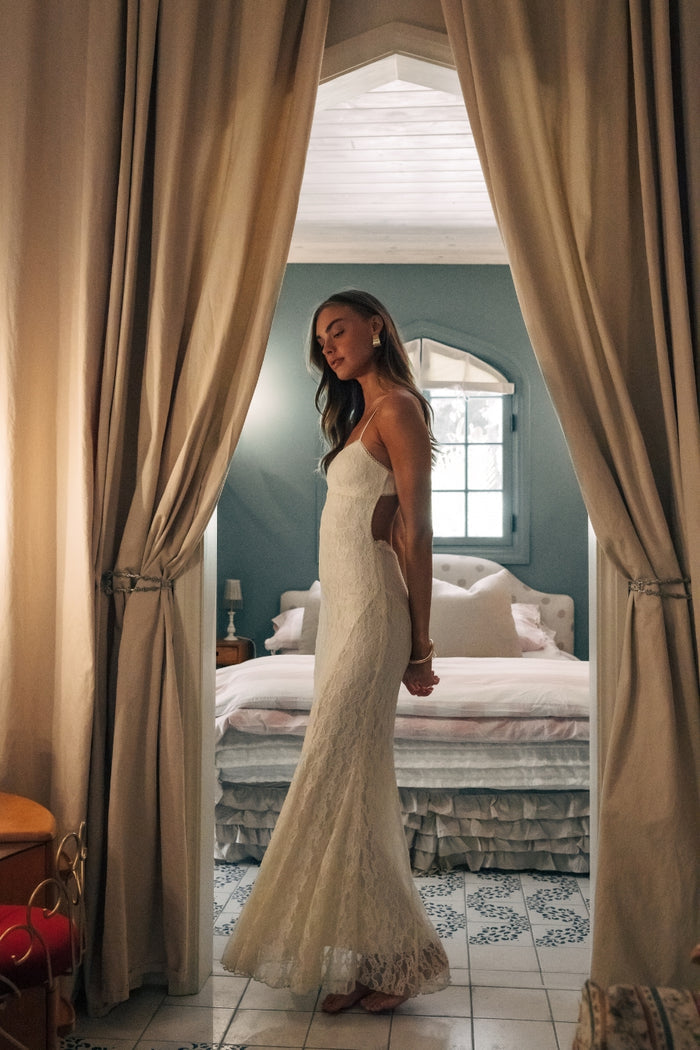 Woman in a white dress standing in a bedroom with curtains open