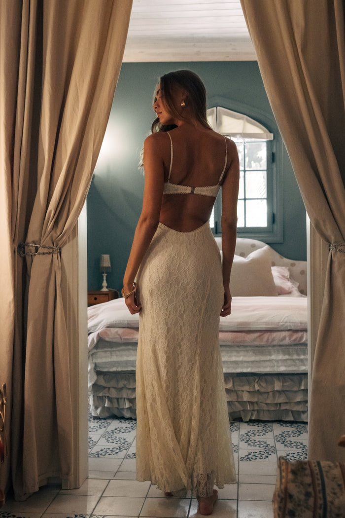 Woman in a beige dress standing in a bedroom with curtains open
