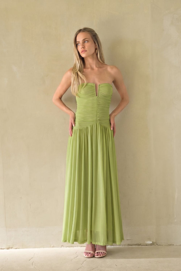 green-image | A woman modeling a strapless lime green maxi dress with a sweetheart neckline and gathered bodice, standing against a textured beige wall.