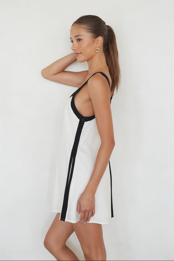 Woman wearing a white dress with black straps against a plain background