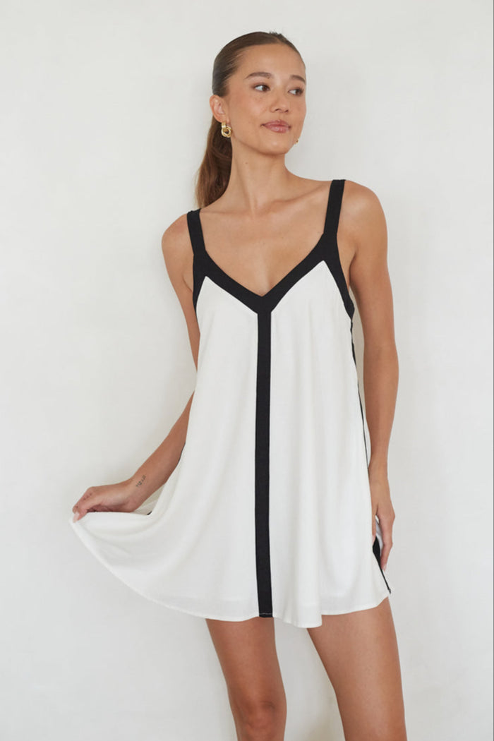 Woman wearing a white dress with black trim on a plain background