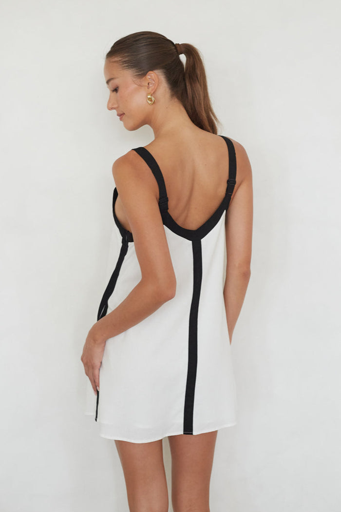 Woman wearing a white dress with black trim against a plain background