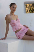 Woman wearing a pink floral dress sitting on a white ledge.