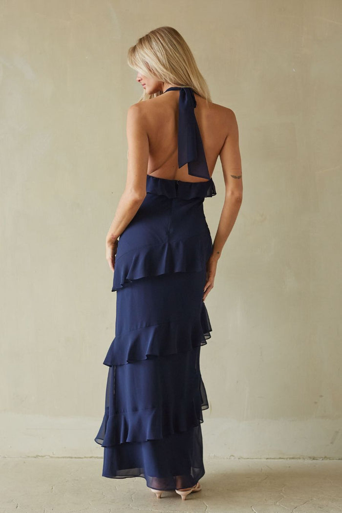Woman wearing a navy blue dress with ruffled layers against a beige background
