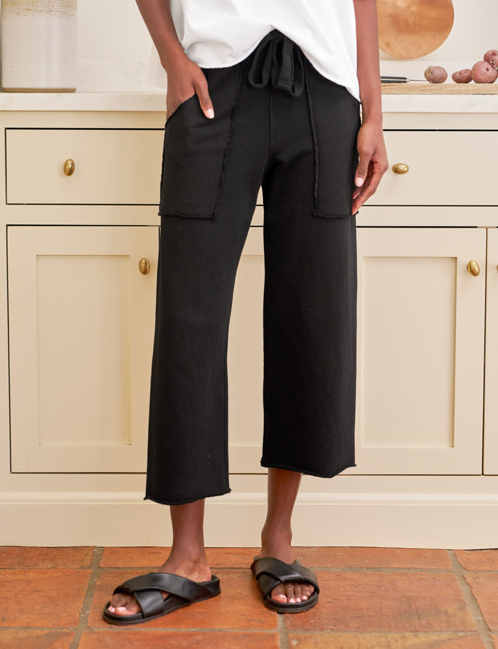 Person wearing black wide-leg pants and white top in a kitchen setting