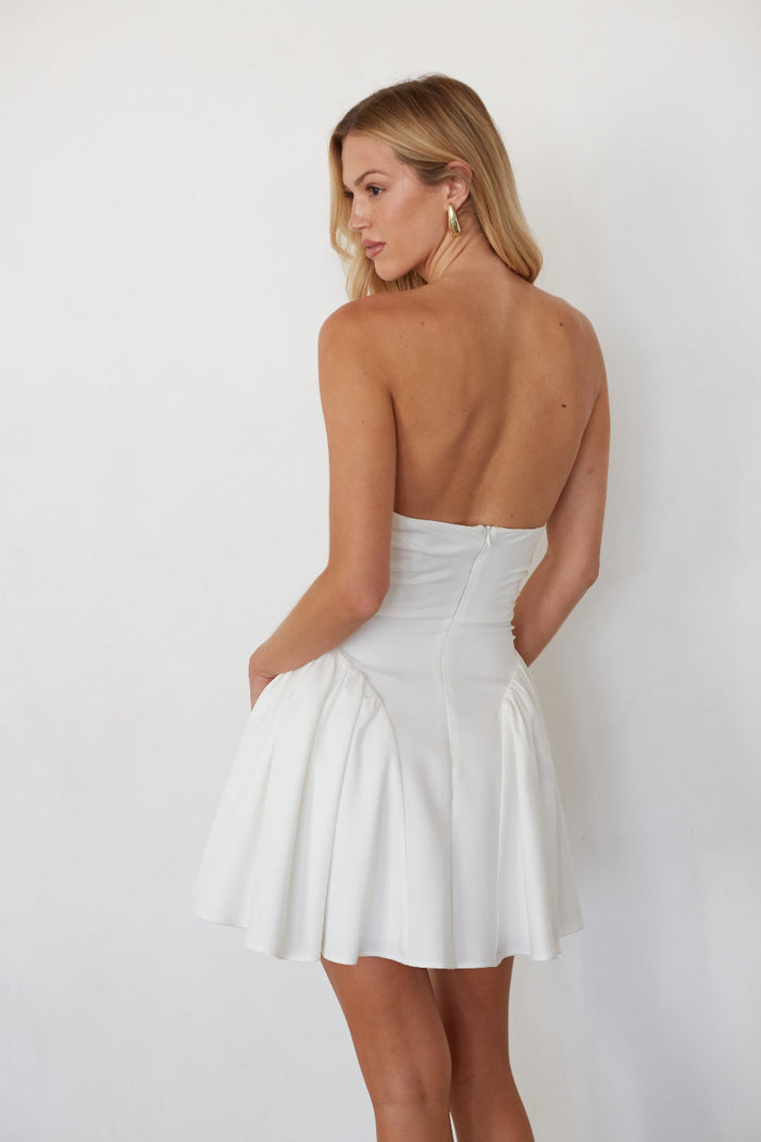 Woman wearing a white strapless dress against a plain background