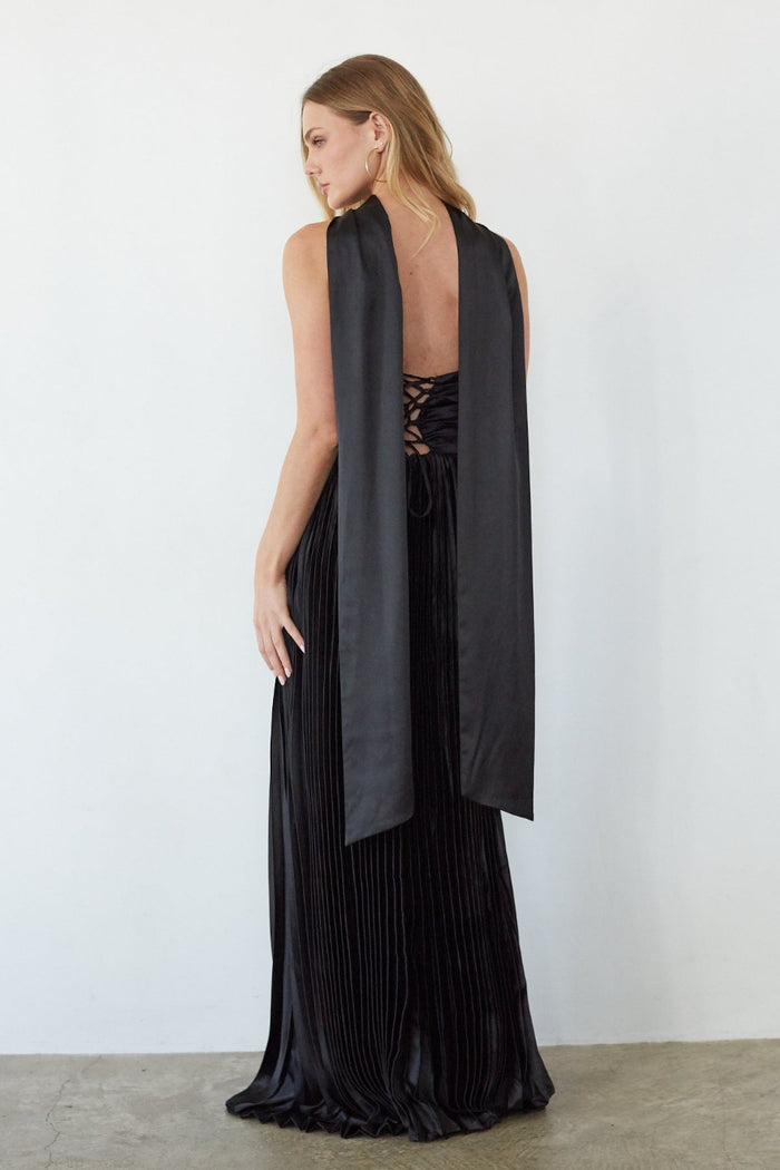 Woman wearing a black pleated dress with a long black vest over a white background