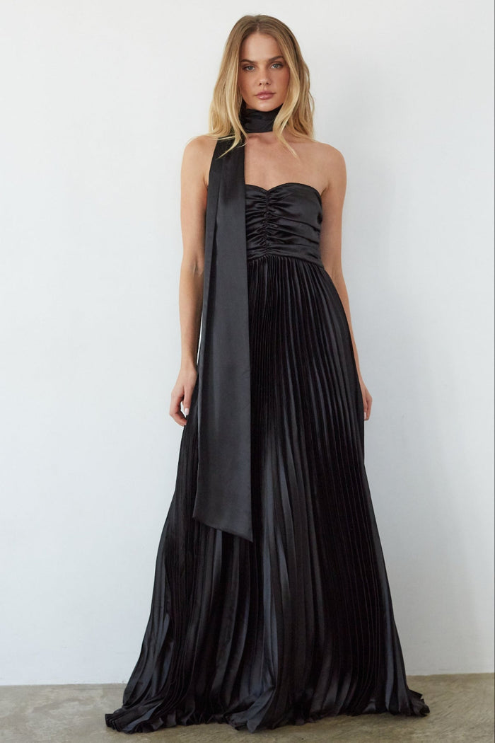 Woman wearing a black pleated evening gown with a long train against a white background