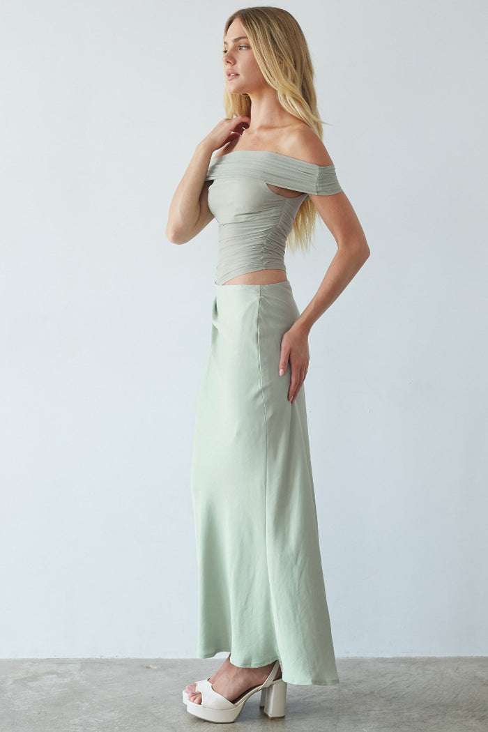 Woman wearing a light green off-shoulder top and wide-leg pants against a white background