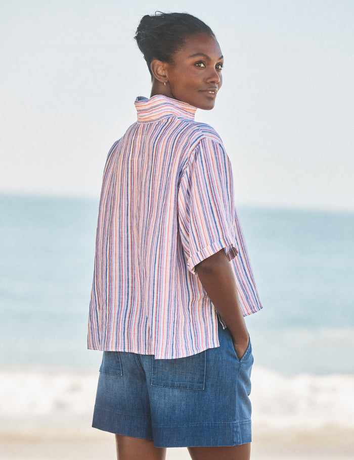 Woman wearing a striped shirt and denim shorts standing on a beach.