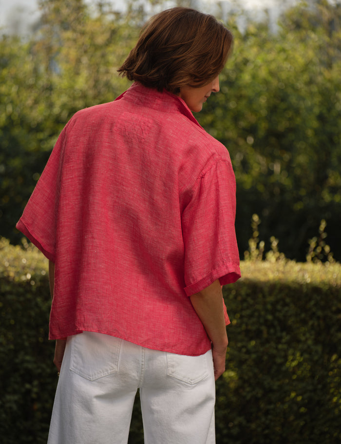 Person wearing a red shirt with a brand logo, standing outdoors with greenery in the background
