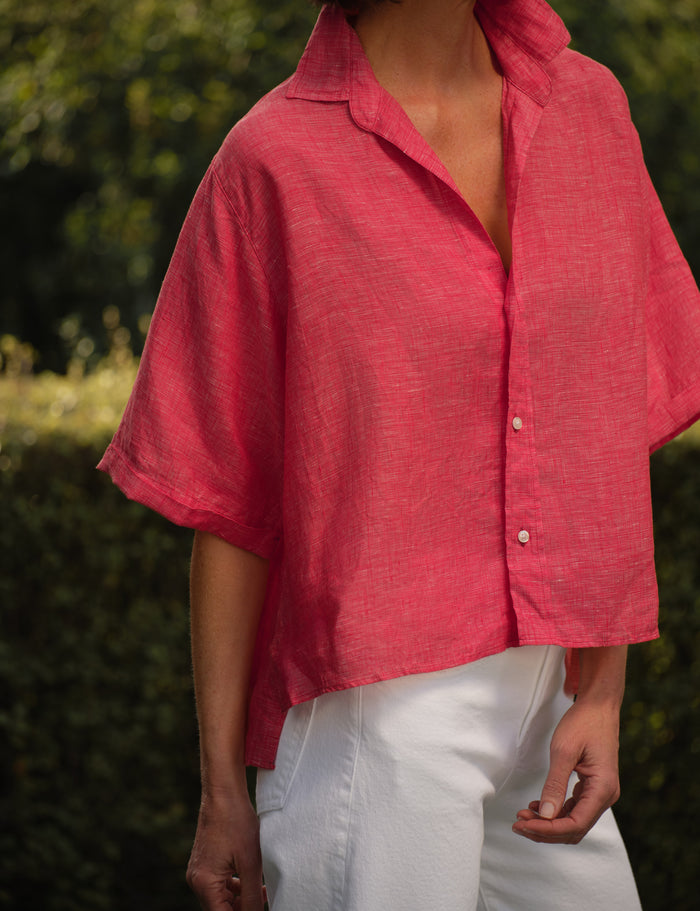 Person wearing a red shirt with short sleeves and white pants outdoors.